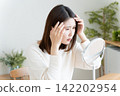 A woman checks her hairline in the mirror. 142202954