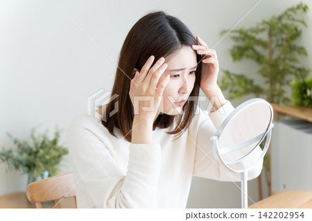 A woman checks her hairline in the mirror. A woman checks her hairline in the mirror. 142202954