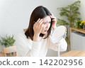 A woman checks her hairline in the mirror. 142202956