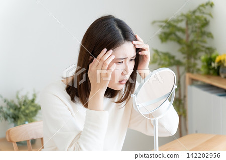 一位女士對著鏡子檢查自己的髮際線。 142202956
