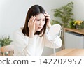 A woman checks her hairline in the mirror. 142202957