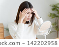 A woman checks her hairline in the mirror. 142202958