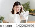 A woman checks her hairline in the mirror. 142202959