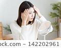A woman checks her hairline in the mirror. 142202961