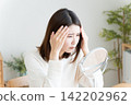 A woman checks her hairline in the mirror. 142202962