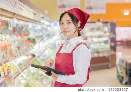 一名女店員正在超市蔬菜區操作平板電腦。 一名女店員正在超市蔬菜區操作平板電腦。 142203367