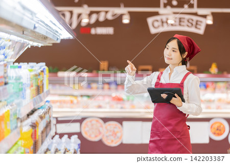 A female employee in the beverage section of a supermarket is holding a tablet to check products. A female employee in the beverage section of a supermarket is holding a tablet to check products. 142203387