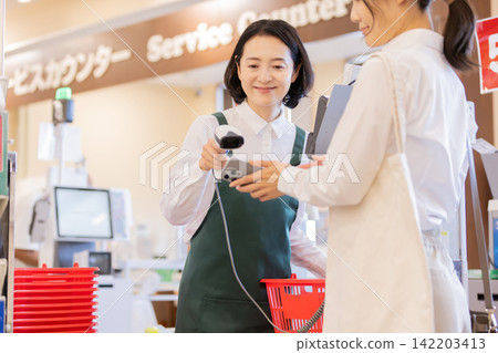A female store clerk at the supermarket checkout counter supports smartphone payments. 142203413