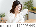 A woman looking in the mirror due to eye problems. 142203445