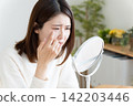 A woman looking in the mirror due to eye problems. 142203446