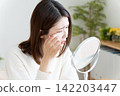 A woman looking in the mirror due to eye problems. 142203447