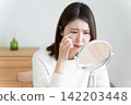A woman looking in the mirror due to eye problems. 142203448