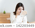 A woman looking in the mirror due to eye problems. 142203449