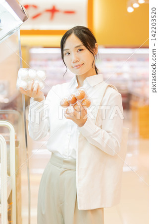 A young woman compares white eggs and brown eggs in the supermarket's egg section to choose one. A young woman compares white eggs and brown eggs in the supermarket's egg section to choose one. 142203520