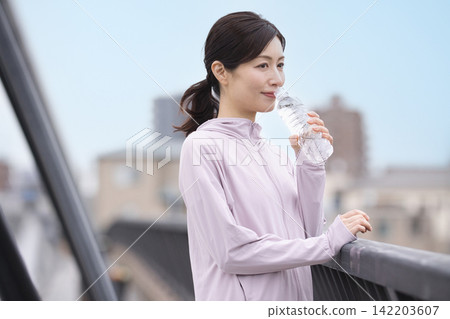 一位中年婦女邊走邊喝瓶裝水。 142203607