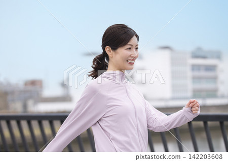 一位中年婦女身穿運動服沿著河岸行走。 一位中年婦女身穿運動服沿著河岸行走。 142203608