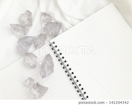 Pale purple natural stones lined up on a white cloth, a lined notebook, healing, record-keeping, power stones. Pale purple natural stones lined up on a white cloth, a lined notebook, healing, record-keeping, power stones. 142204342