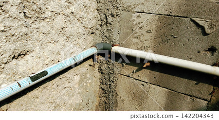 A PVC water pipe elbow fitting installed at the corner of a rough concrete wall. A PVC water pipe elbow fitting installed at the corner of a rough concrete wall. 142204343