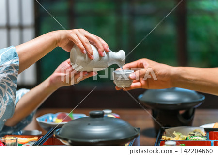 Hands of a man and woman in yukata serving drinks at dinner in a ryokan Hands of a man and woman in yukata serving drinks at dinner in a ryokan 142204660