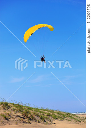 一架動力滑翔傘飛越藍天和沙丘。 一架動力滑翔傘飛越藍天和沙丘。 142204798