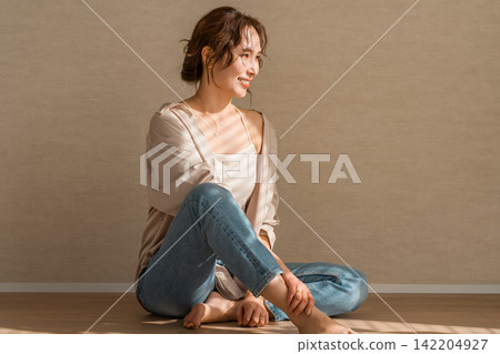 A woman in denim sitting on a wooden floor in the setting sun A woman in denim sitting on a wooden floor in the setting sun 142204927