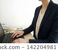 A businesswoman in a suit operating a laptop computer. 142204981
