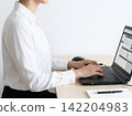 A woman wearing a white shirt is using a computer in an office. 142204983