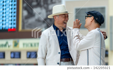 Senior LGBTQ men airport laughter high-five cream suits straw hat Senior LGBTQ men airport laughter high-five cream suits straw hat 142205021