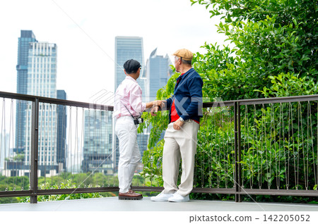 Two senior LGBTQ men converse on modern balcony railing, city skyline and lush greenery behind Two senior LGBTQ men converse on modern balcony railing, city skyline and lush greenery behind 142205052