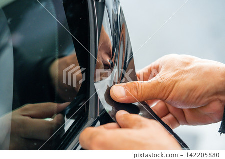 A car wrapping specialist applies a polyurethane film to the car. Detailer PPF A car wrapping specialist applies a polyurethane film to the car. Detailer PPF 142205880