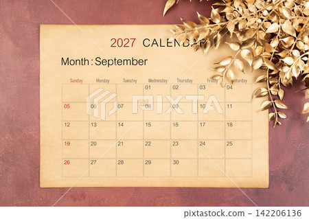 September 2027 calendar page with golden color leaves on red wooden background. September 2027 calendar page with golden color leaves on red wooden background. 142206136