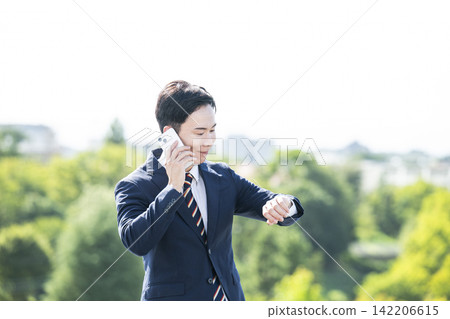 一位商人面帶微笑，一邊打電話一邊看手錶。 142206615