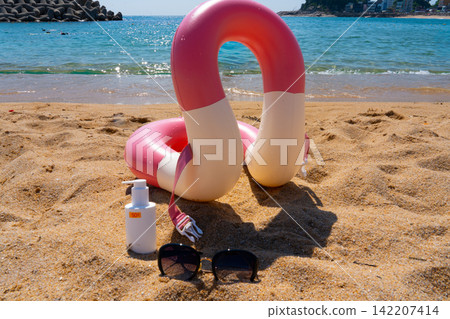 Sunscreen SPF50, sunglasses and swim ring are on the sand by the sea Sunscreen SPF50, sunglasses and swim ring are on the sand by the sea 142207414