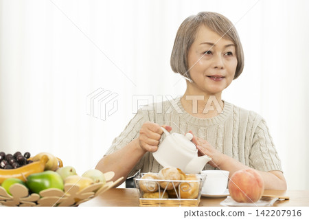 一位老婦人在客廳吃早餐麵包。 一位老婦人在客廳吃早餐麵包。 142207916