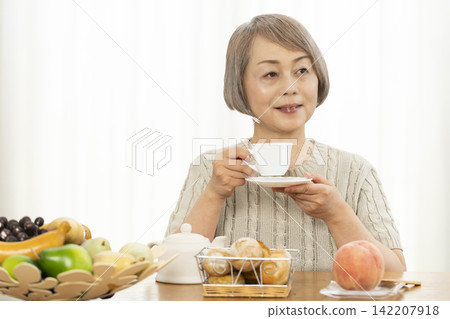 一位老婦人在客廳吃早餐麵包。 一位老婦人在客廳吃早餐麵包。 142207918