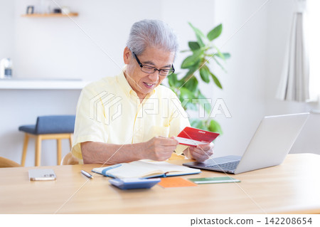 一位老人在客廳看著他的銀行存摺。 一位老人在客廳看著他的銀行存摺。 142208654