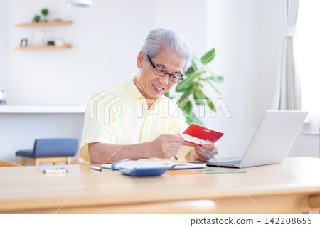 一位老人在客廳看著他的銀行存摺。 一位老人在客廳看著他的銀行存摺。 142208655
