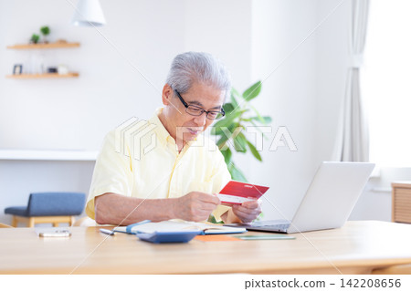 一位老人在客廳看著他的銀行存摺。 一位老人在客廳看著他的銀行存摺。 142208656