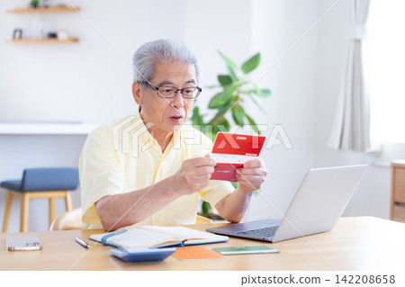 一位老人在客廳看著他的銀行存摺。 一位老人在客廳看著他的銀行存摺。 142208658