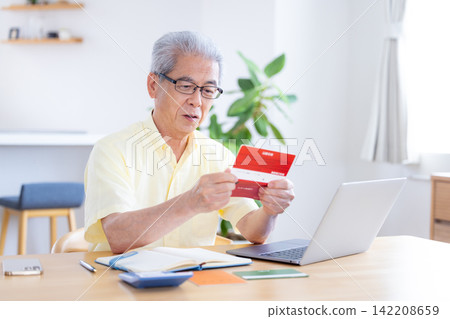 A senior man looking at his bankbook in the living room. A senior man looking at his bankbook in the living room. 142208659