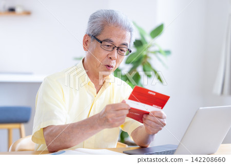 一位老人在客廳看著他的銀行存摺。 一位老人在客廳看著他的銀行存摺。 142208660