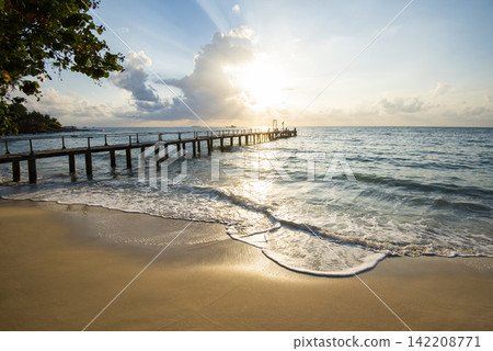 Amazing sandy tropical beach with silhouette wooden bridge out of the beach tropical Boardwalk or Wooden walkway to the horizon on sea ocean paradise landscape , sunrise or sunset sea dramatic sky Amazing sandy tropical beach with silhouette wooden bridge out of the beach tropical Boardwalk or Wooden walkway to the horizon on sea ocean paradise landscape , sunrise or sunset sea dramatic sky 142208771