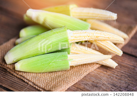 Baby corn on the sack, Fresh young baby corn for cooking health food, Close up raw organic baby corn on wooden background. Baby corn on the sack, Fresh young baby corn for cooking health food, Close up raw organic baby corn on wooden background. 142208848