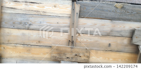 Close-up view of rustic wooden structure made of rough, unpainted horizontal planks. Weathered boards show natural grain patterns, knots, varying shades of light brown and gray with rusty nails Close-up view of rustic wooden structure made of rough, unpainted horizontal planks. Weathered boards show natural grain patterns, knots, varying shades of light brown and gray with rusty nails 142209174