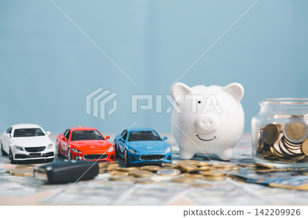 Toy cars, piggy bank, coin jar, car key, and scattered money represent car finance, vehicle comparison, savings, auto loan options, and purchase planning. Toy cars, piggy bank, coin jar, car key, and scattered money represent car finance, vehicle comparison, savings, auto loan options, and purchase planning. 142209926