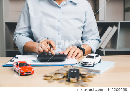 Business person calculating car finance documents with toy cars, car key, coins, and calculator on desk, representing auto loan payment, vehicle insurance, and purchase planning. 142209968