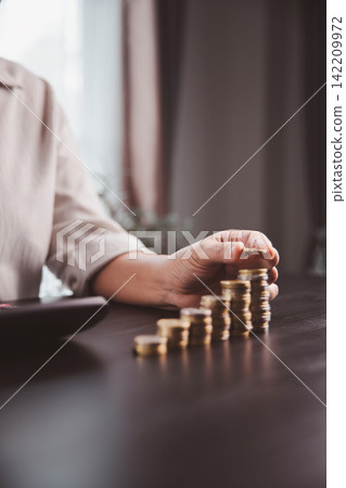 Person placing a coin on the tallest stack beside a laptop, showing savings growth, digital finance, investment planning, income progress, wealth accumulation, and financial success. Person placing a coin on the tallest stack beside a laptop, showing savings growth, digital finance, investment planning, income progress, wealth accumulation, and financial success. 142209972
