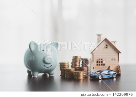 Blue piggy bank, stacked coins, wooden house, and model car represent family savings, home and vehicle goals, asset planning, budgeting, financial security, future prosperity, and copy space. 142209976