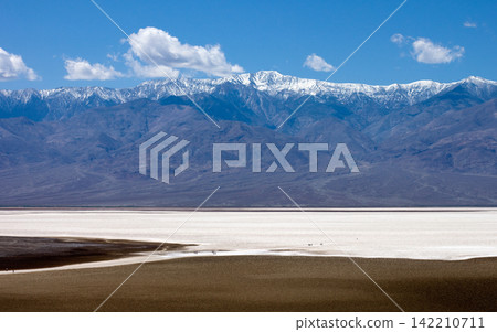 Snowy Mountain Range Over Desert Salt Flat Landscape 142210711