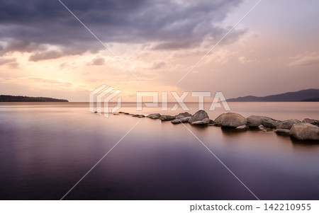 Sunset Seascape with Calm Water, Rocks, and Dramatic Clouds 142210955